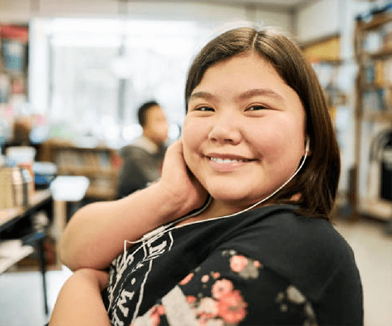 An Indigenous youth smiling, sitting in the classroom setting