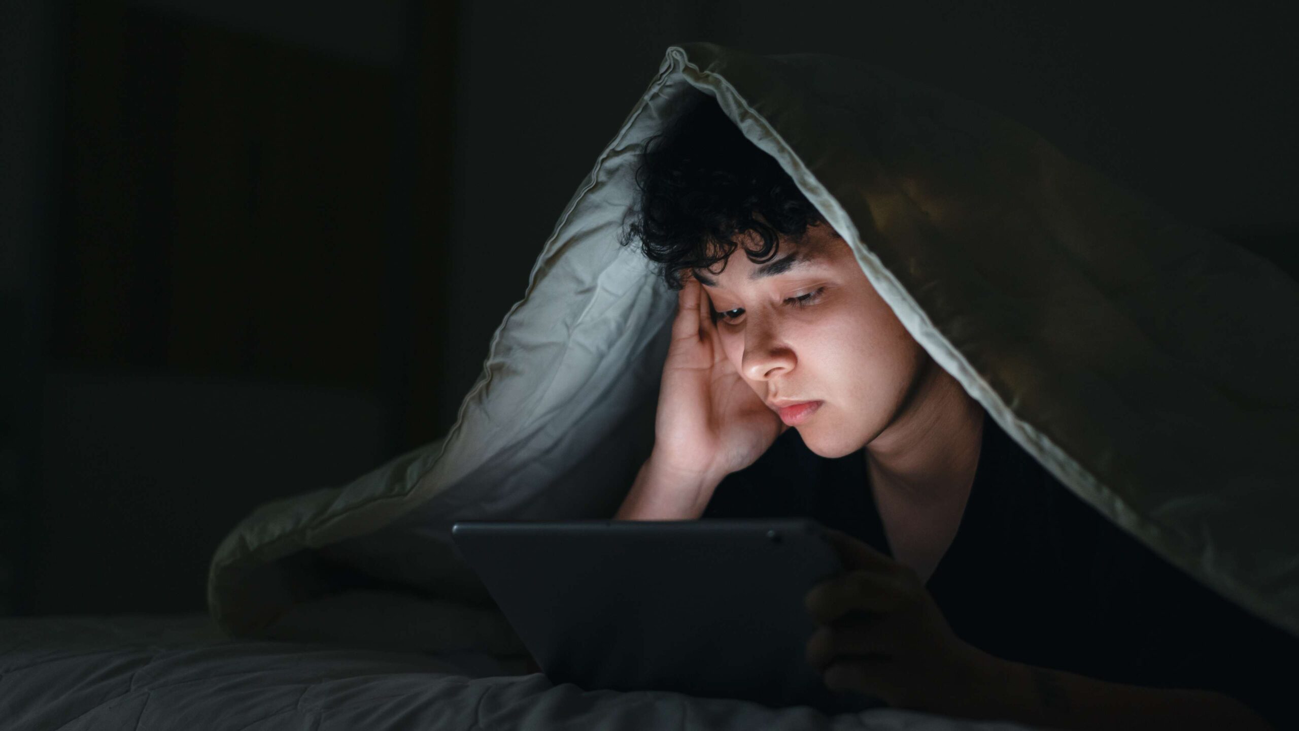 Une image sur une page Web concernant le site Web sur la santé mentale de Jeunesse, J'écoute d’une jeune personne cachée sous une couverture regardant une tablette