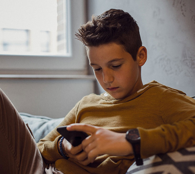Un adolescent assis sur un divan, regardant un téléphone intelligent