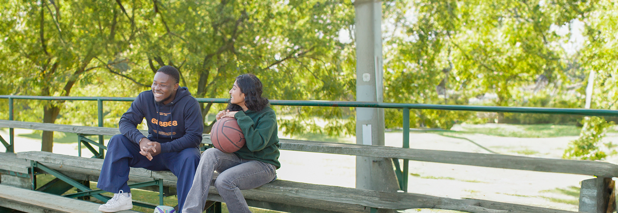 Deux jeunes personnes portant des articles de JJE sont assises dans les gradins avec un ballon de basket