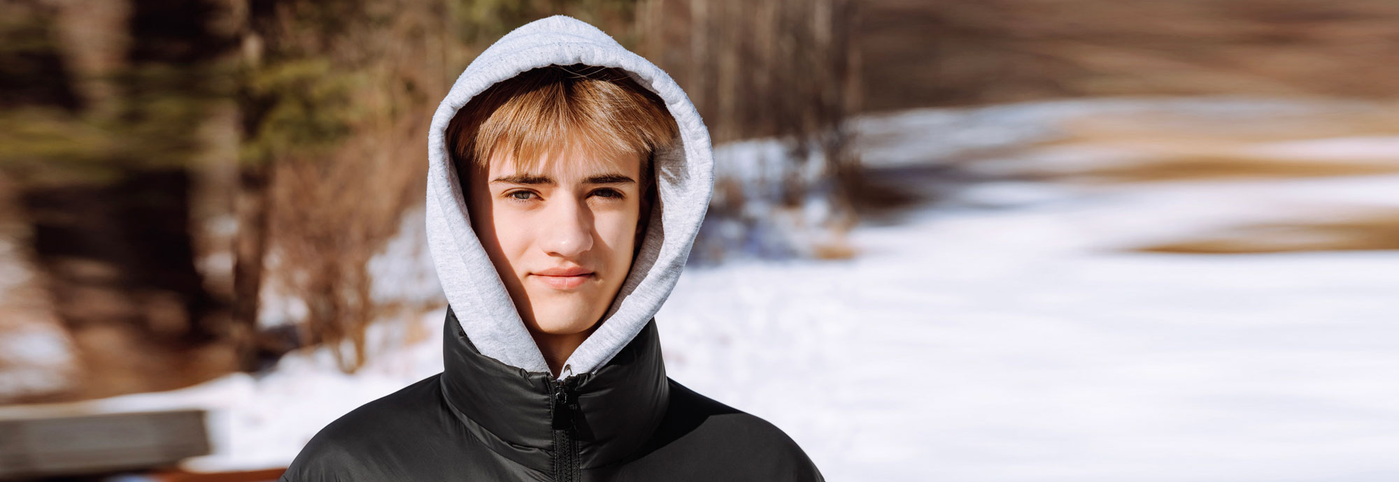 Une jeune personne se tenant à l'extérieur dans la neige, portant un chandail à capuchon et regardant directement dans la caméra.