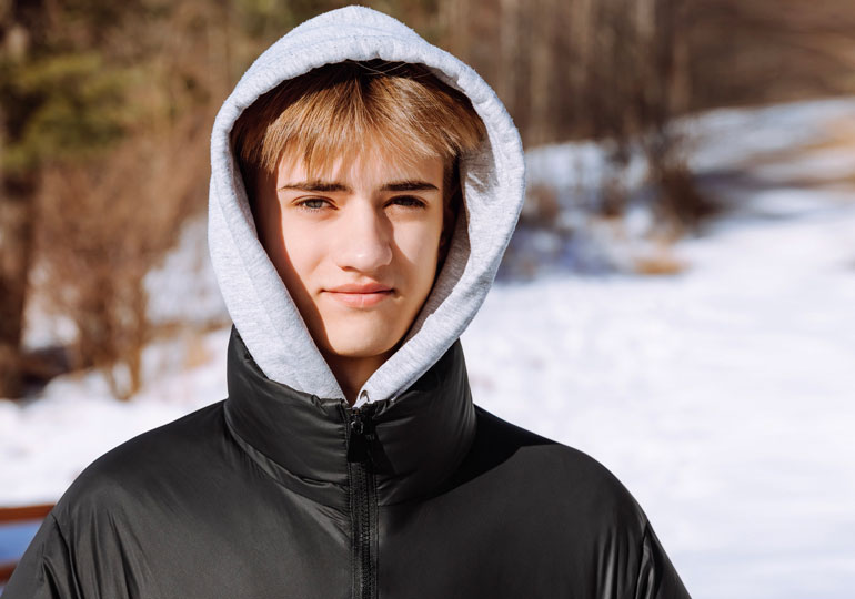 Une jeune personne se tenant à l'extérieur dans la neige, portant un chandail à capuchon et regardant directement dans la caméra.