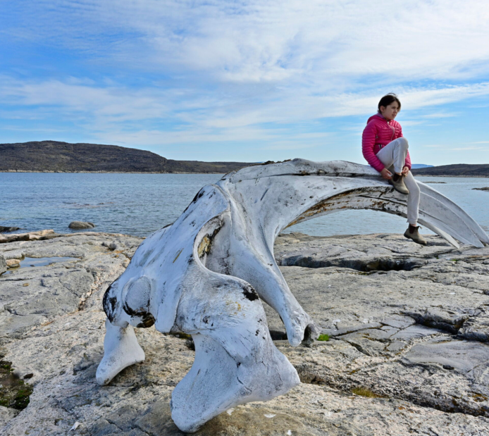 Un·e jeune Inuk perché·e sur un os de baleine, au bord de l’Arctique, sur l’île de Baffin.