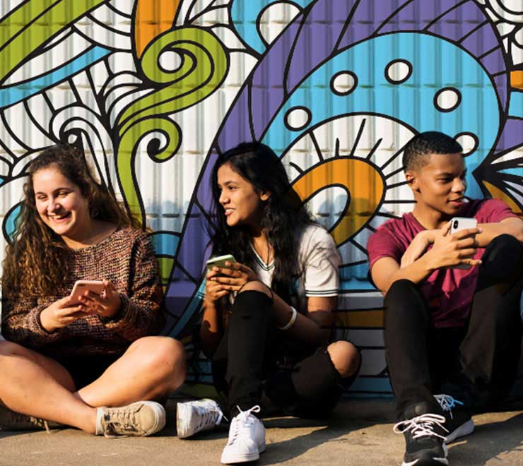 Cinq adolescents clavardent sur leur téléphone, devant un mur avec un dessin