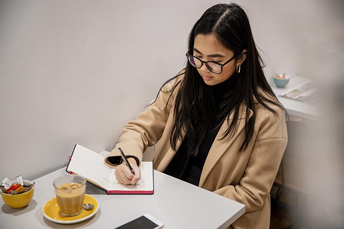 Jeune, assise à une table et écrivant dans un cahier.