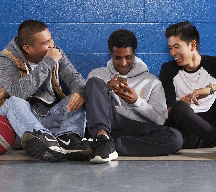 amis adolescents assis dans une salle de gym jouant sur un téléphone et riant