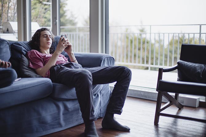 Jeune assis sur un divan et se servant d’un téléphone.