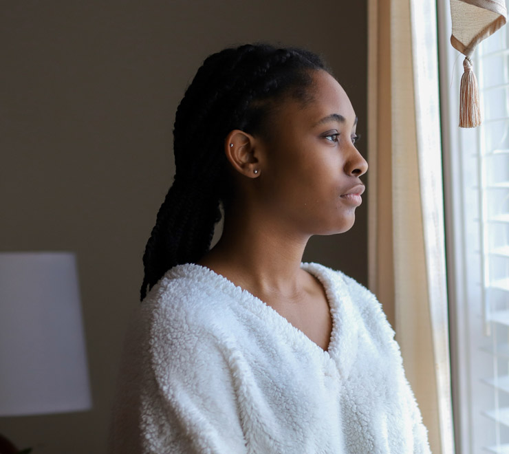 teen at home wearing white sweater and seriously looking through the window