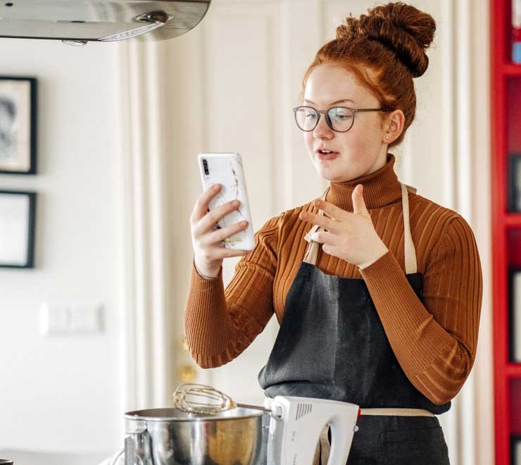 Une adolescente aux cheveux roux qui parle au téléphone tout en cuisinant