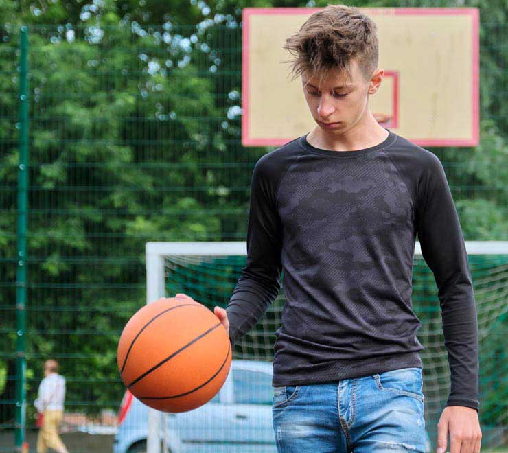 teen bouncing a basketball in an outdoor court