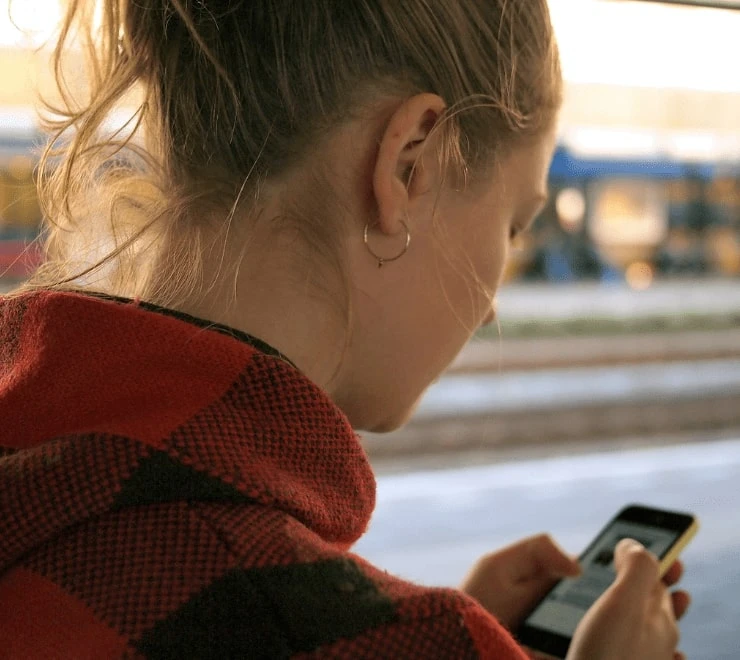 Une jeune personne à l'extérieur utilise un téléphone pour explorer les moyens de faire face à des émotions tels que l'anxiété liée à la guerre et aux conflits